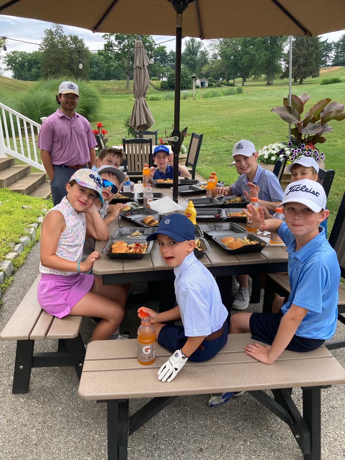 Junior golfers gathered around a picnic table for lunch during summer camp